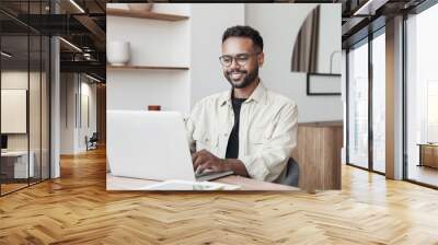 Young man using laptop at home. Businessman or student working on computer online. Freelance, online video conference call, education and technology concept Wall mural