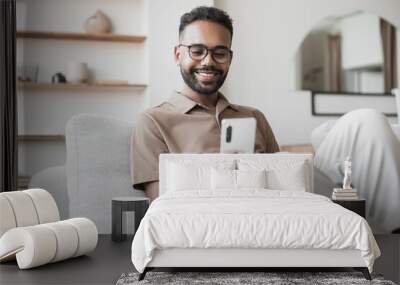 Young man using smartphone at home. Handsome man looking at mobile phone in his room. Communication, social media, connection, mobile apps, technology, modern lifestyle concept Wall mural