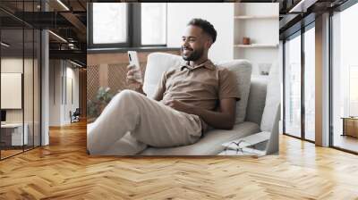 Young man using smartphone at home. Handsome man looking at mobile phone in his room. Communication, social media, connection, mobile apps, technology, modern lifestyle concept Wall mural