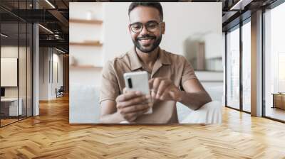 Young man using smartphone at home. Handsome smiling men looking at mobile phone in his room. Communication, home work or study, connection, mobile apps, technology, lifestyle concept Wall mural