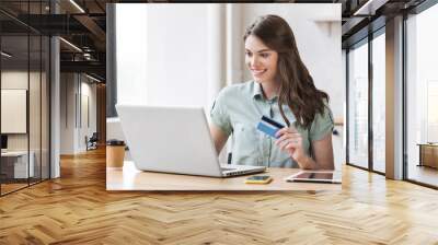 Young woman holding credit card and using laptop computer. Businesswoman or entrepreneur working. Online shopping, e-commerce, internet banking, spending money concept Wall mural