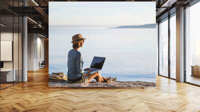 Young woman using laptop computer on a beach. Freelance work concept Wall mural