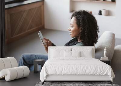 Young woman using smartphone at home. Mixed race girl looking at mobile phone. Communication, social distancing, connection, mobile apps, technology, lifestyle concept Wall mural