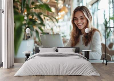 A high-resolution photograph of a young woman marketer, smiling as she works on her laptop in a bright, elegant office setting Wall mural