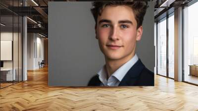 A professional portrait of a young man presenter, captured in a headshot against a neutral backdrop, showcasing his natural charisma and professional demeanor Wall mural