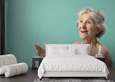 A senior woman presenter with a kind smile, gesturing towards a screen while speaking, set against a solid color background, emphasizing her approachable and engaging style Wall mural