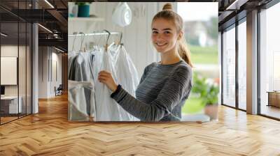 A young woman standing by a drying rack, hanging clothes with care and a smile, enjoying the peaceful routine of doing laundry at home Wall mural