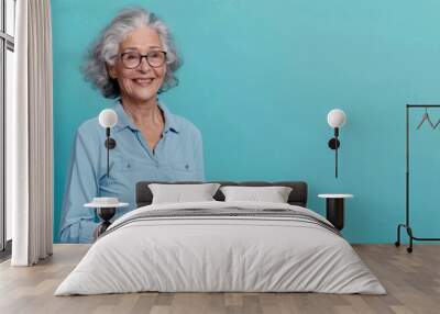 An older woman with a kind smile, holding a tablet while presenting information, set against a solid color background, reflecting her tech-savvy and approachable nature Wall mural