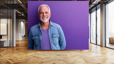 Senior man in casual attire, smiling gently, standing against a solid purple background with space for additional text Wall mural