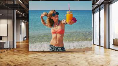 Cute woman drinking juice on the beach. Summer concept. Wall mural