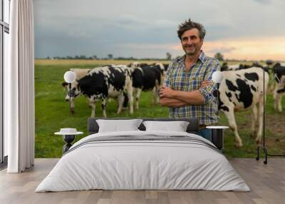 A mature male farmer is smiling in camera proud with his work on a countryside farm with ecologically grown cows used for biological milk products industry. Wall mural