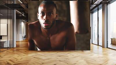 An African American guy trains in a vintage gym and fists his boxing bag fists. Concept of: gym, fitness, boxing, success, workout and power Wall mural