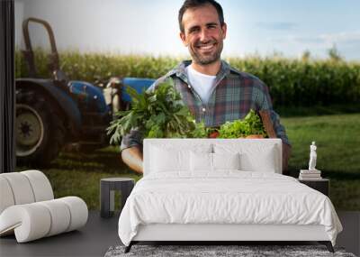 Authentic shot of happy farmer holding basket with fresh harvested at the moment vegetables and smiling in camera on countryside field. Concept:biological, bio products, bio ecology, vegetarian and ve Wall mural