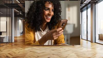 Cinematic close up shot of young happy smiling brazilian woman is using technology smartphone for work or entertainment in living room at home. Wall mural