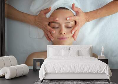 Close up portrait of a beautiful young smiling woman with a towel on her head is receiving a facial massage and spa treatment for perfect skin in a luxury wellness center. Wall mural