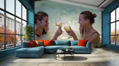 The young happy girl friends are cheering with glasses of fine white wine and having fun in a whirlpool bathtub in a luxury wellness center. Wall mural