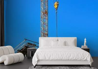 A construction site featuring a tall crane against a clear blue sky, showcasing modern building techniques and urban development. Wall mural