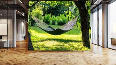 A peaceful hammock hanging between two trees in a lush, green garden, ideal for relaxation and enjoying nature. Wall mural