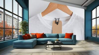 A plain white T shirt is displayed on wooden hanger, featuring clothing tag attached to it. simplicity of design highlights tags potential for branding and style Wall mural