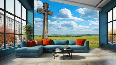 A serene landscape featuring a historic stone cross under a bright blue sky with fluffy clouds and expansive green fields. Wall mural