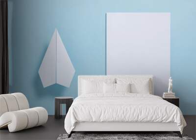 Flat lay of white paper plane and blank paper on pastel blue color background Wall mural