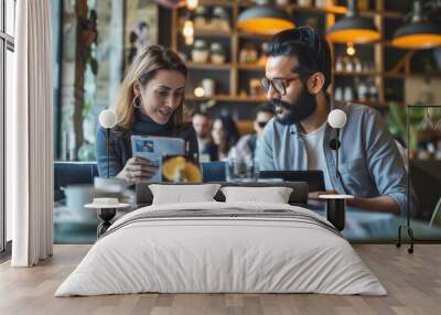 Two people are sitting at a café table, engaged in conversation and looking at documents. Coffee cups are on the table. Wall mural