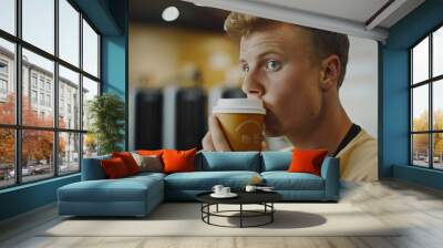 Young man sipping coffee from a to-go cup in a modern indoor setting, looking focused and thoughtful. Wall mural