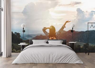 Happy young woman traveler relaxing and looking at the beautiful sunset on the top of mountain Wall mural