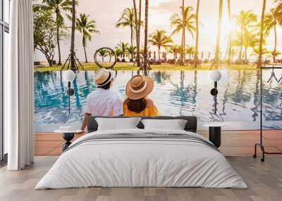 Young couple traveler relaxing and enjoying the sunset by a tropical resort pool while traveling for summer vacation Wall mural