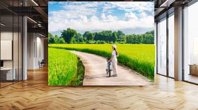 Young happy woman tourist enjoying and riding a bicycle in paddy field while traveling at Nan, Thailand Wall mural