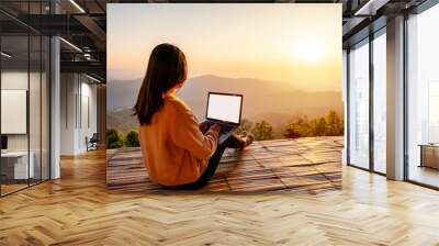 Young woman freelancer traveler working online using laptop and enjoying the beautiful nature landscape with mountain view at sunrise Wall mural