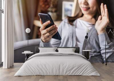 Young woman greeting in a phone video call and sitting on sofa in the living room at home Wall mural