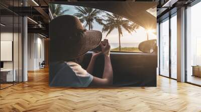 Young woman traveler looking and taking a photo beautiful sunset at the beach inside car Wall mural