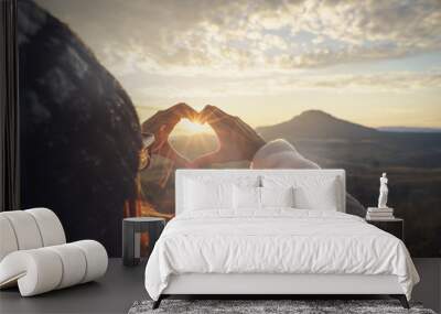 Young woman traveler making heart shape symbol at sunrise Wall mural