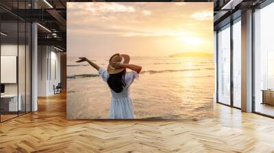 Young woman traveler relaxing and enjoying the beautiful sunset on the tranquil beach, Travel on the summer vacation concept Wall mural