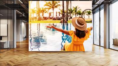 Young woman traveler relaxing and enjoying the sunset by a tropical resort pool while traveling for summer vacation Wall mural