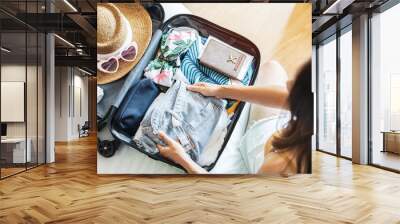 Young woman traveler sitting on the bed packing her suitcase preparing for travel on summer vacation Wall mural