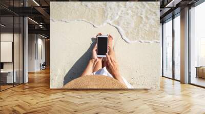 Young woman using mobile phone at beautiful tropical white sand beach with wave foam and transparent sea, Summer vacation and Travel concept with copy space Wall mural