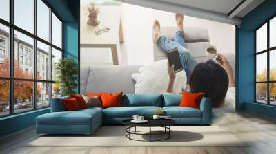 young woman using smartphone at cozy home on sofa in living room Wall mural