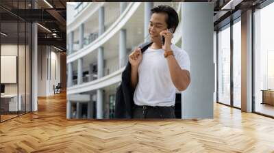 A portrait of a good-looking Asian man holding his suit and standing outdoors Wall mural