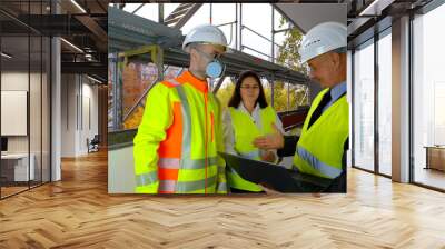 Two men, an architect and construction engineer, foreman and one woman inspect the performance of a project on a laptop, a construction site of a multi-storey house, building in progress Wall mural