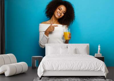 Beautiful smiling african american girl showing a glass of orange juice Wall mural