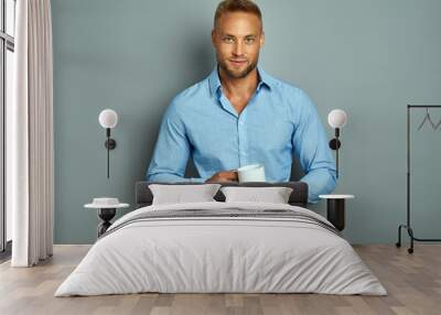 Handsome man in blue shirt looking at camera with a cup Wall mural