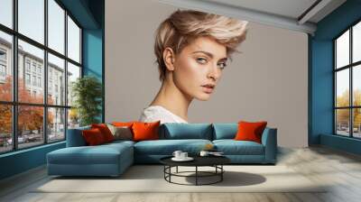 Portrait of young girl with blond fashion hairstyle looking at camera isolated on gray background Wall mural