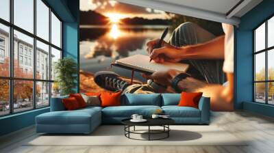 A person writing in a notebook by a lake at sunset captures a moment of inspiration or contemplation, blending natural beauty with creative pursuit. Wall mural