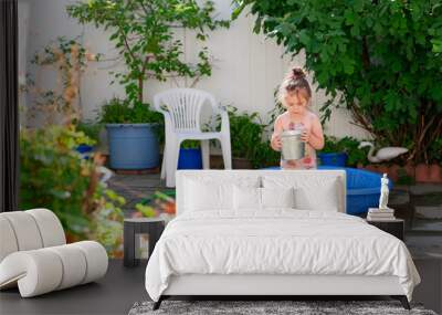 Pretty young girl watering plants with a bucket on a summer day in the backyard Wall mural