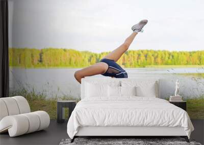 a girl in a swimsuit and sneakers does exercises from rhythmic gymnastics in nature on the river Bank Wall mural