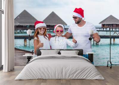 family father and children boy and girl in Santa hats stand on a pier near water villas in the Maldives, concept of winter holidays and luxury travel Wall mural