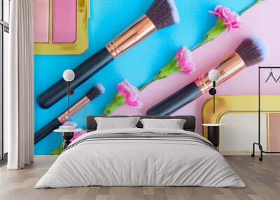 premium makeup brushes, eye shadow palette and flowers on a colored blue and pink background, creative cosmetics flat lay with diagonal composition Wall mural