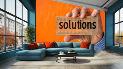 hand holding a business card with the word 'solutions' printed on a vibrant orange background Wall mural